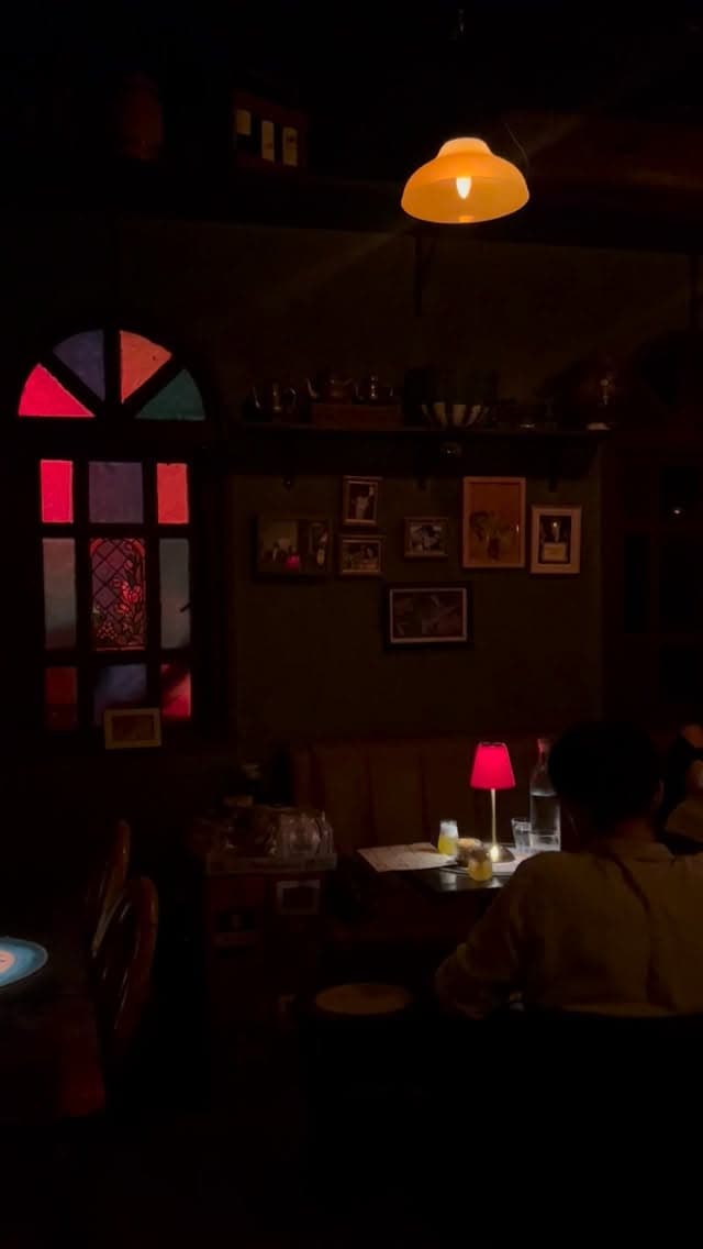 The dimly lit Oriental Elixir room with stained glass, framed pictures, and red table lamps