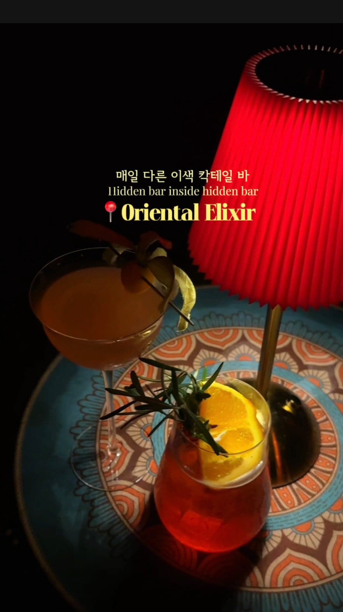 Three colourful cocktails on a patterned table beside a red lamp